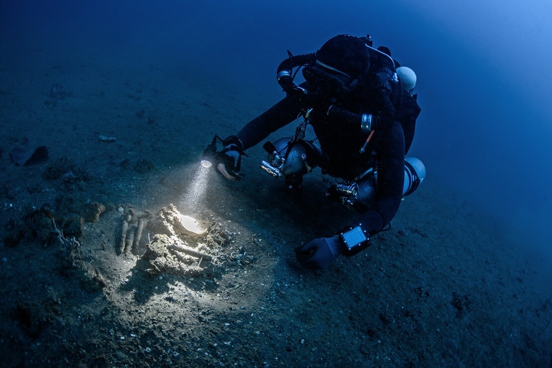 Taucher am Meeresgrund leuchtet mit einer Taschenlampe auf dem Sand